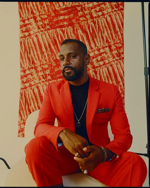 Man in orange suit sitting with orange backdrop